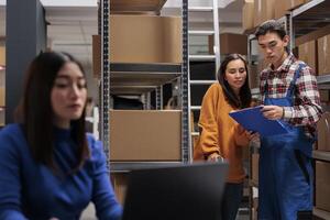 Delivery managers analyzing customer orders list clipboard in ecommerce retail business warehouse. Storehouse asian man and woman employees checking inventory report data in storage room photo