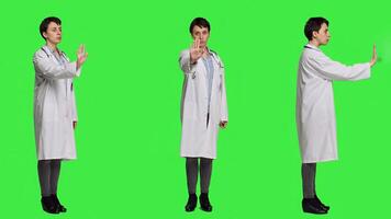 Woman physician raising palm and doing stop sign in studio, expressing rejection and denial against greenscreen backdrop. General practitioner showing warning symbol with negative reaction. Camera A. photo