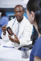 de cerca de un africano americano médico explicando diagnóstico y tratamiento a el caucásico mujer mientras participación un botella de medicamento. hembra paciente recepción salud cuidado consulta. foto