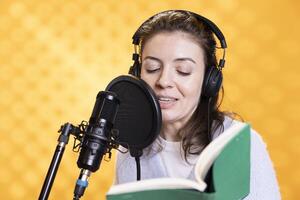 sonriente dama haciendo narración leyendo de libro a Produce audio libro. contento voz actor utilizando cuentacuentos habilidades a entretener audiencia mientras productor digital grabación de novedoso, estudio antecedentes foto