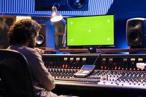 Sound engineer working with isolated display in studio control room, pushing buttons and sliders to produce beats. Audio technician creating music by editing tracks in post production. photo