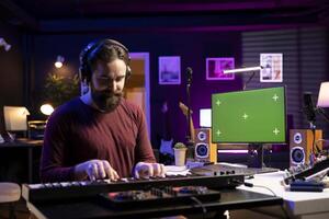 Audio engineer playing piano electronic keyboard notes in home studio, learning to play midi controller by watching tutorials on greenscreen pc. Musician hitting synthesizer keys for a song. photo