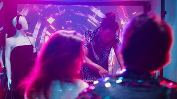 Cool man using DJ mixing station at club, creating funky music beats for crowd of people in discotheque. Men and women having fun dancing with disco lights and live sound. Handheld shot. photo