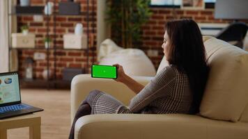 Remote employee looking at green screen smartphone while optimizing market performance charts. Teleworker checking online business analytics statistical data metrics on mockup mobile phone and laptop photo