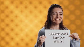 Portrait of happy woman holding placard with world book day message written on it, isolated over studio background. Geek promoting importance of reading during 23th April global event, camera A photo