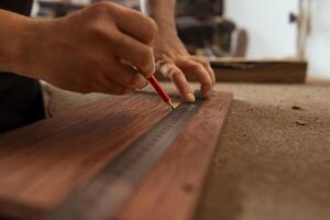 Craftsperson using ruler to take measurements of plank used to make wood furniture in carpentry shop. Woodworking expert drawing with pencil on wooden board to determine where to make cut, close up photo