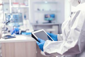 CLose up of medical researcher using tablet pc in laboratory dressed in ppe. Team of scientists conducting vaccine development using high tech technology for researching treatment against covid19 photo