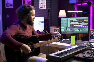 Musician learning to tune his guitar with internet tutorial via greenscreen on phone, twisting the knobs and practicing music lessons. Artist songwriter does rehearsal with acoustic instrument. photo