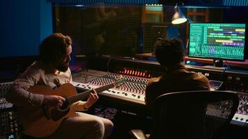 Rockstar recording music on his guitar in professional studio, creating new music for his album in control room. Artist composer producing tracks on electro acoustic guitar. Camera B. photo