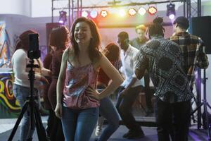 alegre sonriente mujer tomando foto en teléfono inteligente mientras teniendo divertido en Club nocturno. despreocupado riendo niña grabación utilizando móvil teléfono en trípode mientras ir de fiesta en club