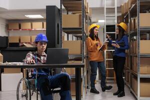 Warehouse worker in wheelchair planning delivery on laptop in logistics and distribution center storage room. Young asian storehouse employee with disability analyzing clients orders checklist photo