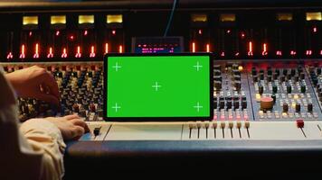 Audio expert mixing and mastering tunes on editing software next to greenscreen tablet, producing and recording tracks by pushing buttons and faders. Sound engineer in control room. Camera A. photo