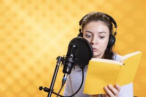 Narrator with shocked look on face reading horror book, recording audiobook using microphone, studio background. Woman with fearful facial expression producing digital recording of novel photo