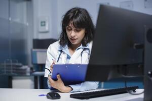 Close-up shot of female practitioner writing medical notes on her clipboard. Detailed image of a caucasian doctor dedicatedly reviewing information from patient consultations. photo