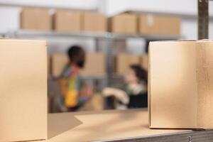 Selective focus of cardboard boxes in warehouse, in background diverse team preparing customers packages for delivery. Storage room employees discussing online orders, checking shipping detalis photo