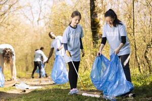 dulce niño y madre coleccionar basura y el plastico en un disposición bolsa, reciclaje basura y limpieza el bosque ecosistema. joven niña trabajando con su mamá a ordenado arriba el naturaleza. foto