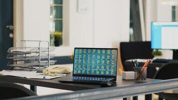 Company documents and laptop in financial department office showing stock exchange values. Business files on desk next to notebook showing forex trading indexes prices, panning shot photo