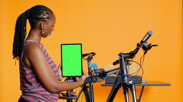 mujer sostiene verde pantalla tableta, utilizando eso a anunciar bicicleta reparar comercio, vacío marcador de posición para empresa logo, estudio antecedentes. mecánico promoviendo bicicleta fijación Servicio con Bosquejo dispositivo, cámara si foto