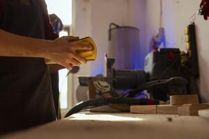 Woodworker working in carpentry shop using sanding block to remove imperfections on wood piece. Carpenter using coarse grade sandpaper to do manual sanding, close up shot photo