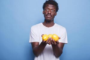africano americano masculino individual que lleva limones y mirando a el cámara. negro hombre participación y demostración amarillo, agrios frutas para vitaminas, nutrición, y sano estilo de vida. foto