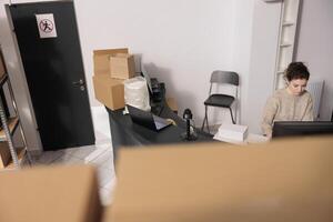 Top view of supervisor standing at counter desk, analyzing merchandise logistics on computer. Storage room worker checking clients online orders preparing packages for delivery photo