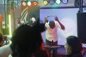 DJ vistiendo auriculares en etapa con focos durante concierto En Vivo actuación en club. músico poniendo en auriculares mientras mezcla electrónico música a disco fiesta en Club nocturno foto