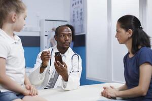 caucásico madre y hija atentamente escuchando a un africano americano médico describiendo el botella de medicamento. ellos discutir salud cuidado con un énfasis en completo evaluación y tratamiento. foto