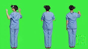 Medical assistant uses interactive vr glasses to check disease treatment, looking at patient examination files with virtual reality headset and lens. Nurse against greenscreen backdrop. Camera A. photo