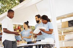 Diverse group united by charity, assisting the needy, donating food and offering support to homeless people. Volunteers supporting hunger relief initiative, providing free warm meals to the poor. photo