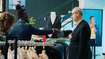Fashion stylist making trendy recommendations for senior client, pairing an expensive tie to match a black elegant shirt. African american worker selling designer items to man. Camera A. photo