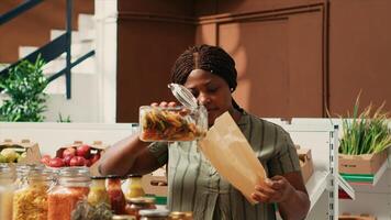 Woman client filling in paper bag with pasta sold as bulk item, buying various types of organic additives free products from local farmers market. Buyer searching for bio pantry supplies. photo