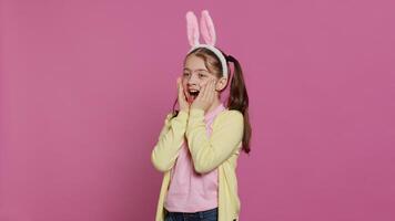 Adorable surprised schoolgirl being in shock after seeing something in studio, smiling and feeling very happy. Joyful small child with bunny ears being amazed by gifts. Camera A. photo