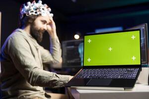 Focus on green screen laptop used by developer wearing EEG headset device translating thoughts into PC commands. IT professional controlling computer functions using mind, helped by mockup notebook photo