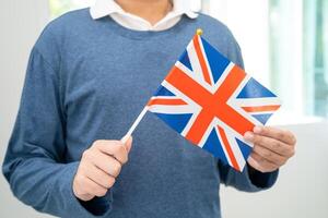 aprender Inglés idioma, asiático Adolescente estudiante sostener Reino Unido bandera en curso a escuela. foto