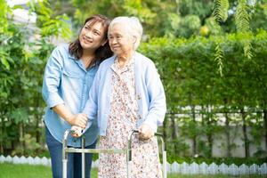 Doctor caregiver help and care Asian senior woman patient walk with walker in park at hospital. photo