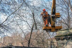 Dnepr, Ukraine - 03.20.2024 Municipal service workers stand with a chainsaw in a crane basket and trim dangerous trees photo