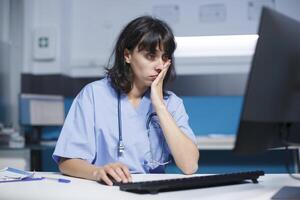 In office, medical assistant uses a computer and mouse for the healthcare system. While working late at night, the nurse is glancing at the monitor screen for support and assistance. photo