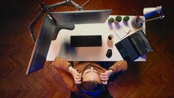 Top down view of technician puts headphones on while fortifying firewalls, teleworking for IT company. Computer scientist listening music and upgrading binary code scripts in home office, aerial shot photo