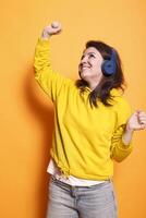 contento persona bailando y escuchando a música en auriculares en estudio. positivo mujer sensación relajado y haciendo danza se mueve mientras utilizando auriculares a disfrutar sonidos y canción terminado naranja antecedentes. foto