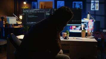 Software developer putting face in hands in frustration while updating binary code script on computer, receiving errors. Admin in apartment exasperated by annoying bugs while programming, camera B photo