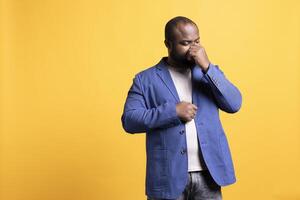 African american man blowing nose after catching cold during winter, isolated over studio background. BIPOC person suffering from flu, having trouble with sinus infection photo