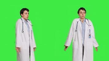 Physician being uncertain about something in studio, shrugging and feeling clueless about the right answer. Doctor doing i dont know symbol against greenscreen backdrop, confusion. Camera B. photo