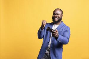 Happy BIPOC gamer celebrating after winning gaming console game, studio background. Euphoric man bragging after being victorious in game, defeating all enemies using gamepad photo