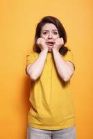 retrato de temeroso morena dama posando para el cámara con su manos en su caras. aterrorizado mujer lata ser Escuchó gritando y temblor en el estudio. emocional adulto quien es asustado. foto