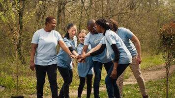 alegre orgulloso equipo de activistas unirse efectivo a limpiar un bosque, celebrando su trabajar como voluntario trabajo por conectando manos juntos. contento personas demostración responsabilidad para el ambiente. cámara una. foto