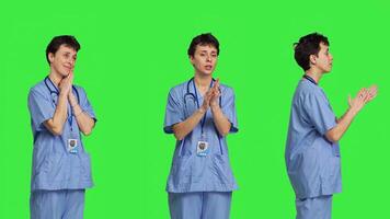Smiling medical assistant applauding someone in studio, celebrating success and cheering against greenscreen backdrop. Young nurse clapping hands and feeling happy about achievement. Camera B. photo
