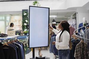 African american woman browsing footwear collection using smart display in fashion boutique. Shopping center customer checking shoes brand promotion on interactive blank screen photo