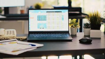 Stock market diagrams with charts and stock figures on laptop sitting on desk in empty workplace. Trading index listings displayed on notebook screen in financial department, panning shot photo