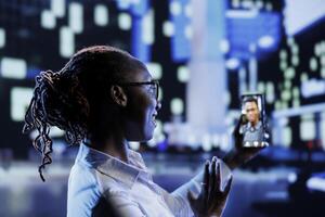 Woman in videocall with coworker while strolling around city streets at night, talking about her day at work. Citizen using smartphone to show workplace colleague surroundings in town center photo