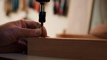 Woodworker using power drill to create holes for dowels in wooden board, close up. Carpenter sinks screws into wooden surfaces with electric tool, doing precise drilling for seamless joinery, camera A photo